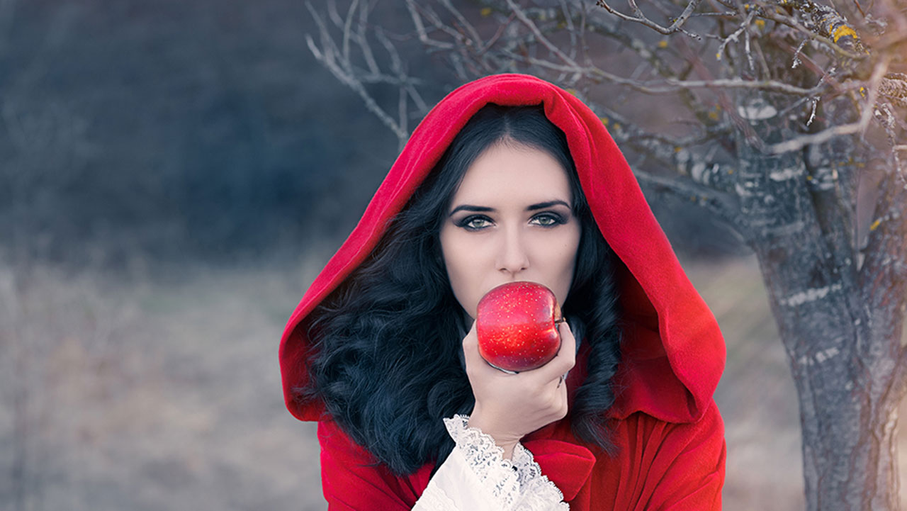 A beautiful woman with a red cloak is about to bite a red apple