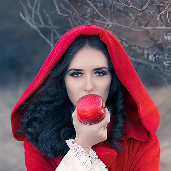 A beautiful woman with a red cloak is about to bite a red apple